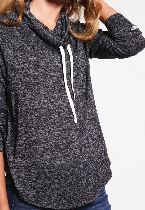 Gråmelange sweatshirt med cowl-neck, med vita snörningar och långa ärmar, bärs med blå jeans mot en enfärgad bakgrund.