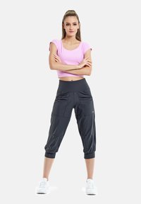 Top corto rosa chiaro abbinato a pantaloni atletici grigio scuro a sigaretta con tasche e polsini elasticizzati. Tessuto liscio, design aderente.