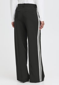 Pantaloni neri a gamba larga con strisce bianche sui lati, caratterizzati da una finitura liscia, passanti per la cintura e tasche posteriori discrete.
