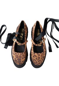 Zapatos de piel de leopardo hechos de ante con una suela de goma negra. Presentan una correa en el tobillo con una hebilla rectangular y cordones largos negros.