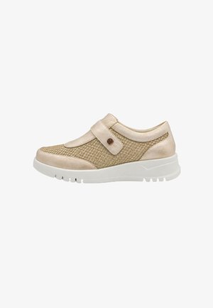 Zapatilla deportiva beige de mujer con tejido texturizado, una amplia correa con detalle de botón y una suela gruesa de goma blanca.