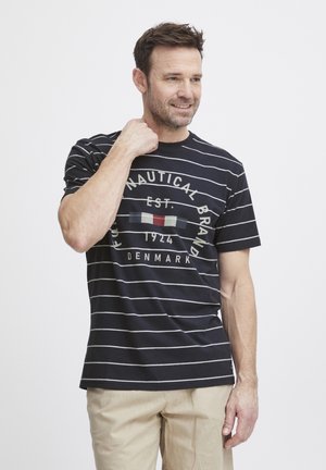 Navy striped t-shirt with short sleeves, cotton material, featuring a printed logo in muted colors, worn with light beige pants.