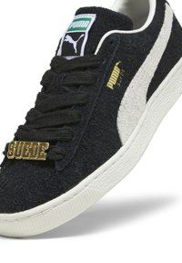 Baskets en daim noir avec une bande blanche, accent doré "SUÉDE" sur les lacets et semelle en caoutchouc blanc texturé. Logo Puma sur la languette.