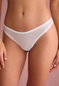 White sheer thong with contrasting elastic waistband, featuring a smooth texture and minimalistic design. Close-up view of fabric draping.