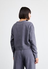 Sudadera de felpa con cuello redondo en gris oscuro, que presenta un ajuste relajado, hombros caídos y puños acanalados con un acabado suave y texturizado.