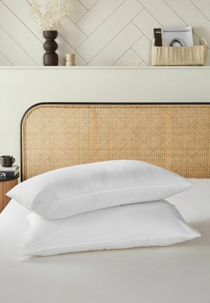 Zwei weiße Kissen auf einem Bett gestapelt mit einem geflochtenen Rattan-Kopfteil und neutraler Dekoration, einschließlich Vasen und Zeitschriften in einem Korb.