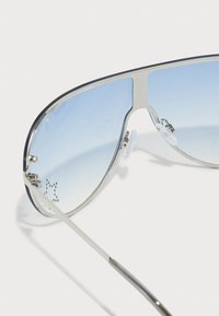 Silberne metallische Flieger-Sonnenbrille mit gradienten blauen Gläsern, ausgestattet mit verstellbaren Nasenpads und dezenten perforierten Details im Rahmen.