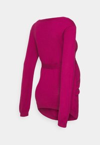 Długi rękaw bluzki ciążowej w kolorze fuksji, z dopasowanym fasonem, marszczonymi detalami po bokach i okrągłym dekoltem. Miękka dzianinowa tekstura.