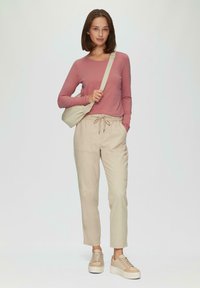 Langärmliges rosefarbenes Oberteil kombiniert mit beigen Jogginghosen mit Kordelzug und beige Plattform-Sneakern. Enthält eine passende kleine Umhängetasche.