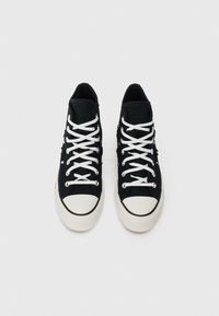 Mustad mustatsi kingad valgete varvaste ja valgete nööbiga, vaadatud ülaltpoolt valgel taustal.