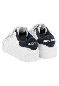 Zapatillas de cuero blancas con un acento texturizado en azul marino en el talón. En la parte trasera dice "QUE TENGAS UN BUEN DÍA" en letras blancas. Suela de goma plana.