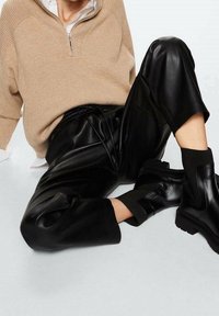 Beżowy sweter dzianinowy z kołnierzykiem na zamek, w zestawieniu z czarnymi spodniami z sztucznej skóry i czarnymi botkami za kostkę z prążkowanymi akcentami i masywną podeszwą.
