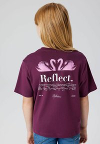 Bordowa koszulka z okrągłym dekoltem, krótkimi rękawami oraz różowym graficznym wzorem łabędzia z tyłu. Tekst podkreśla samorefleksję i naukę.