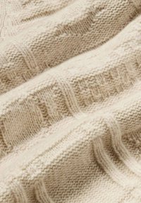 Tissu tricoté de couleur crème avec un motif texturé, comportant des rayures en relief et des sections côtelées, présentant une apparence douce et confortable.