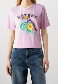 Short-sleeve, pastel pink T-shirt made of cotton, featuring a colorful toucan, floral graphics, and the word "NATURE" in bold letters.