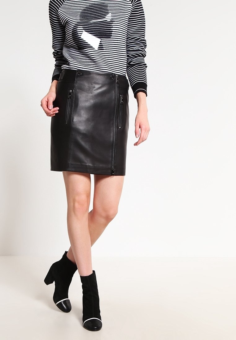 Svart läderkjol med framfickor med dragkedja, knälång, i kombination med en randig tröja och svarta ankelstövlar med vita accenter.