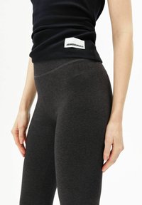 High-waisted, donkergrijze legging gemaakt van zachte, rekbare stof. Heeft een gladde textuur en een merkembleem op de tailleband.