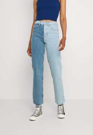 Person wearing high-waist two-tone jeans, dark blue sleeveless crop top, and black-and-white patterned high-top sneakers.