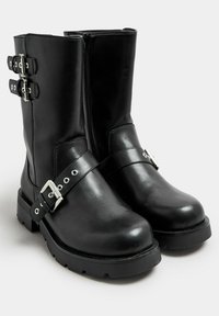 Botas de tobillo de cuero negro con hebillas plateadas a los lados, una superficie lisa, puntera redonda y una resistente suela de goma negra.