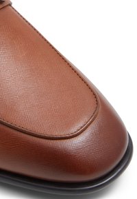 Ruskeat nahkakengät, joissa on teksturoitu pinta, pyöreä kärki, brodeeratut yksityiskohdat ja musta pohja, jotka esittelevät sulavaa ja hienostunutta muotoilua.