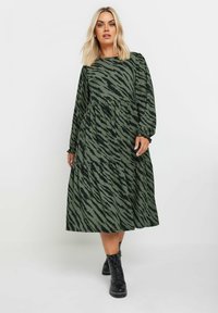 Grön midiklänning med ett tigerstripemönster. Har långa ärmar, rund halsringning och en lager-på-lager kjol. Matchad med svarta kängor.