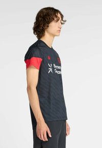 Camiseta deportiva negra con mangas cortas rojas, tela texturizada, cuello redondo y logotipo impreso en el frente. Presenta un diseño de corte ajustado.