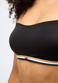 Μαύρο σουτιέν χωρίς τιράντες με λεία υφή, διαθέτει μια ταινία με χρυσές, λευκές και ναυτικές ρίγες, και ένα μικρό λογότυπο «BOSS» στο μπροστινό μέρος.