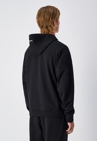 Sudadera negra con textura suave, que cuenta con una capucha con cordón, puños y dobladillos acanalados. La parte posterior tiene un acento reflectante en el cuello.
