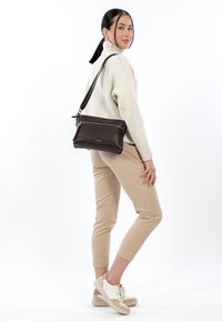 Borsa a tracolla in pelle marrone con finitura testurizzata, scomparti con zip e tracolla regolabile. Su sfondo neutro.