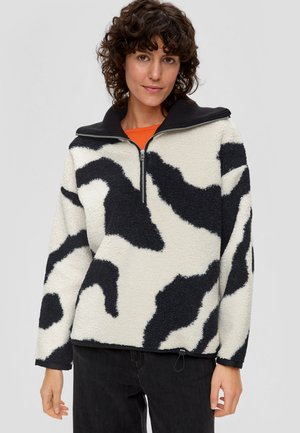 Polarowy półgolf w odcieniu off-white z czarnym nadrukiem w krowie plamy, z zamek przy kołnierzu, długimi rękawami i lekko ściągniętym dołem.