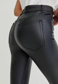 Leggings de cuero sintético negro con cintura alta, diseño ajustado, bolsillos planos y detalles de costura sutiles. Textura suave y apariencia elegante.