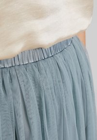 Top color beige chiaro con texture morbida, abbinato a una gonna di tulle blu chiaro a strati con una vita elastica arricciata.