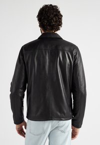 Zwarte leren jas met een platte kraag, een gladde structuur en een aansluitend ontwerp, voorzien van naden langs de rug en mouwen.