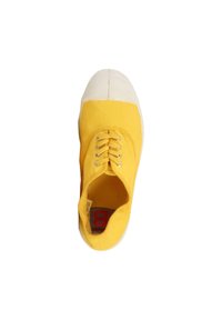 Zapatilla de lona amarilla con puntera y suela de goma blanca, vista desde arriba sobre un fondo blanco.