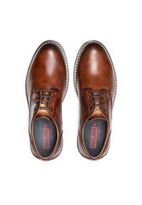 Zapatos de cuero marrón con punta redondeada, diseño de cordones y costuras blancas en contraste. El interior presenta un logo rojo sobre una plantilla negra.