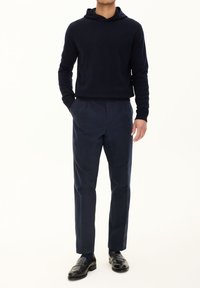 Granatowy sweter z kapturem, zestawiony z granatowymi spodniami o dopasowanym kroju i czarnymi mokasynami, tworzy spójną monochromatyczną stylizację.
