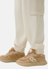 Beige sneakers met een textuur van bont en suede accenten, gecombineerd met crèmekleurige joggers met taps toelopende pijpen enGathered cuffs.