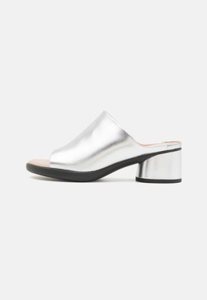 Sølvfarvet mule med åben tå, lav blokhælhæl og sort sål, med en glat metallisk overdel og slip-on-design.