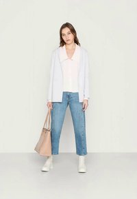 Blazer azul claro sobre uma blusa rosa claro, combinado com jeans azul claro e botas de tornozelo brancas. Segurando uma mala tote bege.