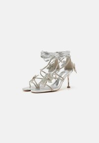 Sandales à talons hauts argentées avec des brides entrecroisées, des embellissements floraux avec des rhinestones et une finition métallique texturée.