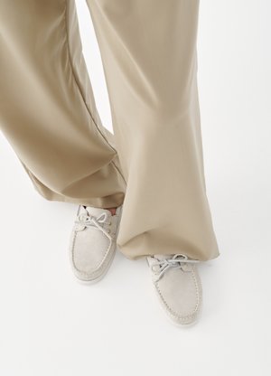 Mocassins en daim beige avec lacets portés avec un pantalon ample marron clair sur un fond blanc uni.