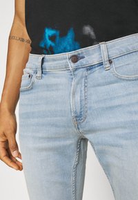 Ljusblå denimjeans har en slim fit, en knappstängning och subtila blekningar. Synliga sömmar framhäver den övergripande designen.