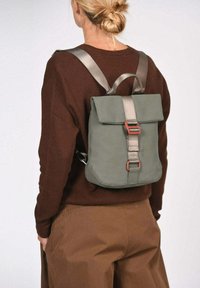 Sac à dos rectangulaire vert avec rabat replié, bretelles grises et éléments décoratifs rouges ; fabriqué en matériau lisse et durable.