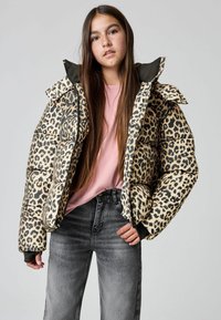 Polsteret jakke med leopardprint og høj krave, prydet med kontrasterende sorte detaljer, båret over en pink t-shirt og grå jeans.