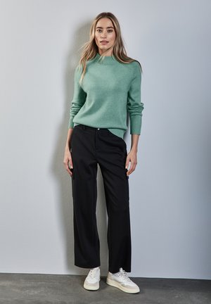 Pull en maille vert menthe avec col côtelé, associé à un pantalon noir ample et des baskets blanches, sur fond gris clair.