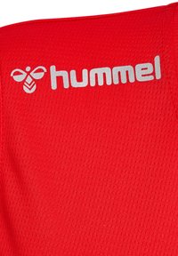 Rode sporttrui van textuurstof, met het witte "hummel" logo. Het ontwerp bevat een bij-embleem boven de merknaam, in het midden van de borst.