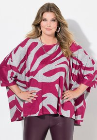 Top oversize a righe magenta e grigio in un tessuto morbido, con scollatura ampia e maniche a pipistrello, abbinato a leggins scuri.