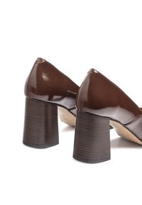 Chaussures en cuir verni marron avec un bout pointu et un talon en bois épais. Le talon présente une texture côtelée, ajoutant du détail au design.