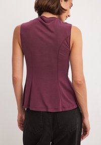 Bezramionkowa burgundowa bluzka z dopasowanym korpusem i rozkloszowanym dołem. Miękka tekstura, okrągły dekolt oraz subtelne detale szwów na plecach.