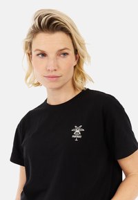 Zwarte katoenen t-shirt met een witte palmboom graphic en de tekst "PROTEST" eronder. Ronde hals, korte mouwen. Soepele textuur.